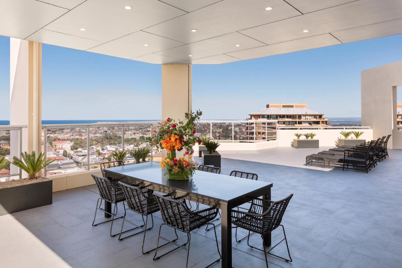 Meriton Suites Bondi Junction Sydney Luaran gambar The photo shows a stylish outdoor terrace or balcony area, featuring a long dining table surrounded by several black wire chairs. The table has a centerpiece of vibrant flowers. The space is well-lit, with a clear view of the horizon in the backgroun