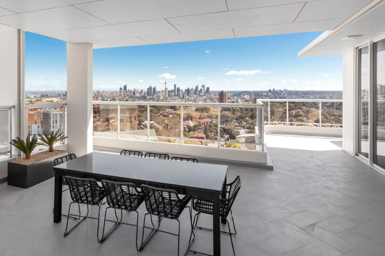 Meriton Suites Bondi Junction Sydney Luaran gambar The photo shows a modern outdoor balcony or terrace space with a dining table and chairs. The table is black and has a minimalist design, surrounded by stylish chairs. In the background, there is a stunning view of a city skyline under a clear blue s