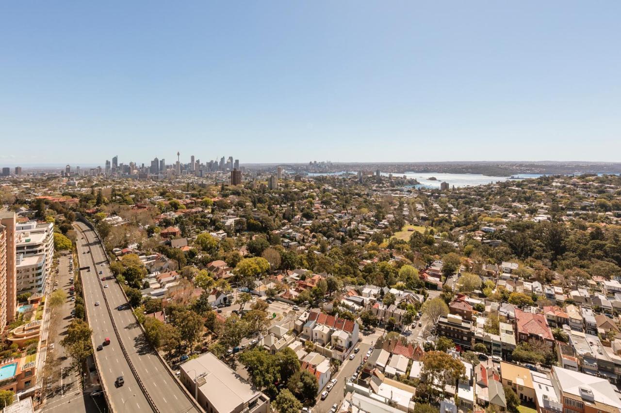 Meriton Suites Bondi Junction Sydney Luaran gambar The photo captures a panoramic view of a vibrant urban landscape. In the foreground, there are residential areas with various houses and greenery, showcasing a suburban environment. In the background, the skyline of a city can be seen, featuring tall