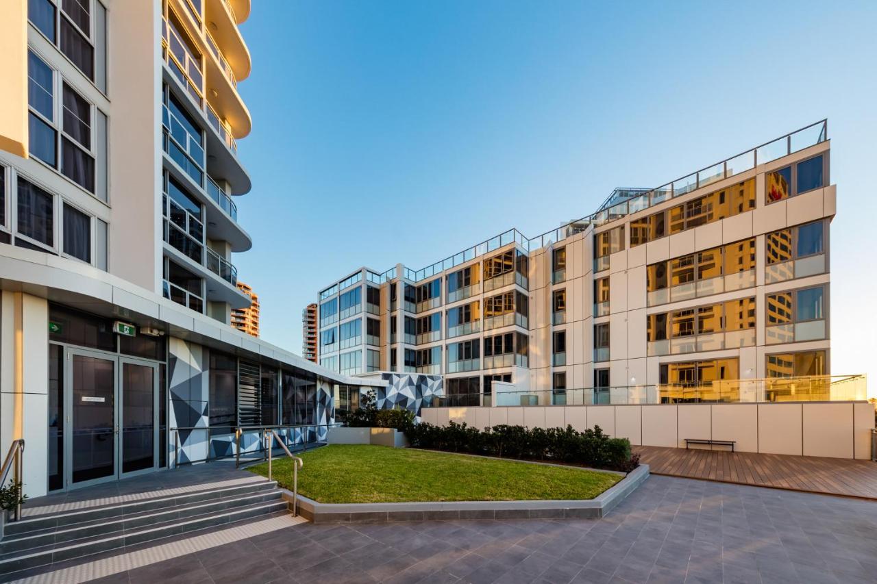 Meriton Suites Bondi Junction Sydney Luaran gambar The photo showcases a modern residential area featuring contemporary buildings. In the foreground, there is a landscaped green space surrounded by well-designed architecture. The buildings have large glass windows, reflecting the light, and feature a