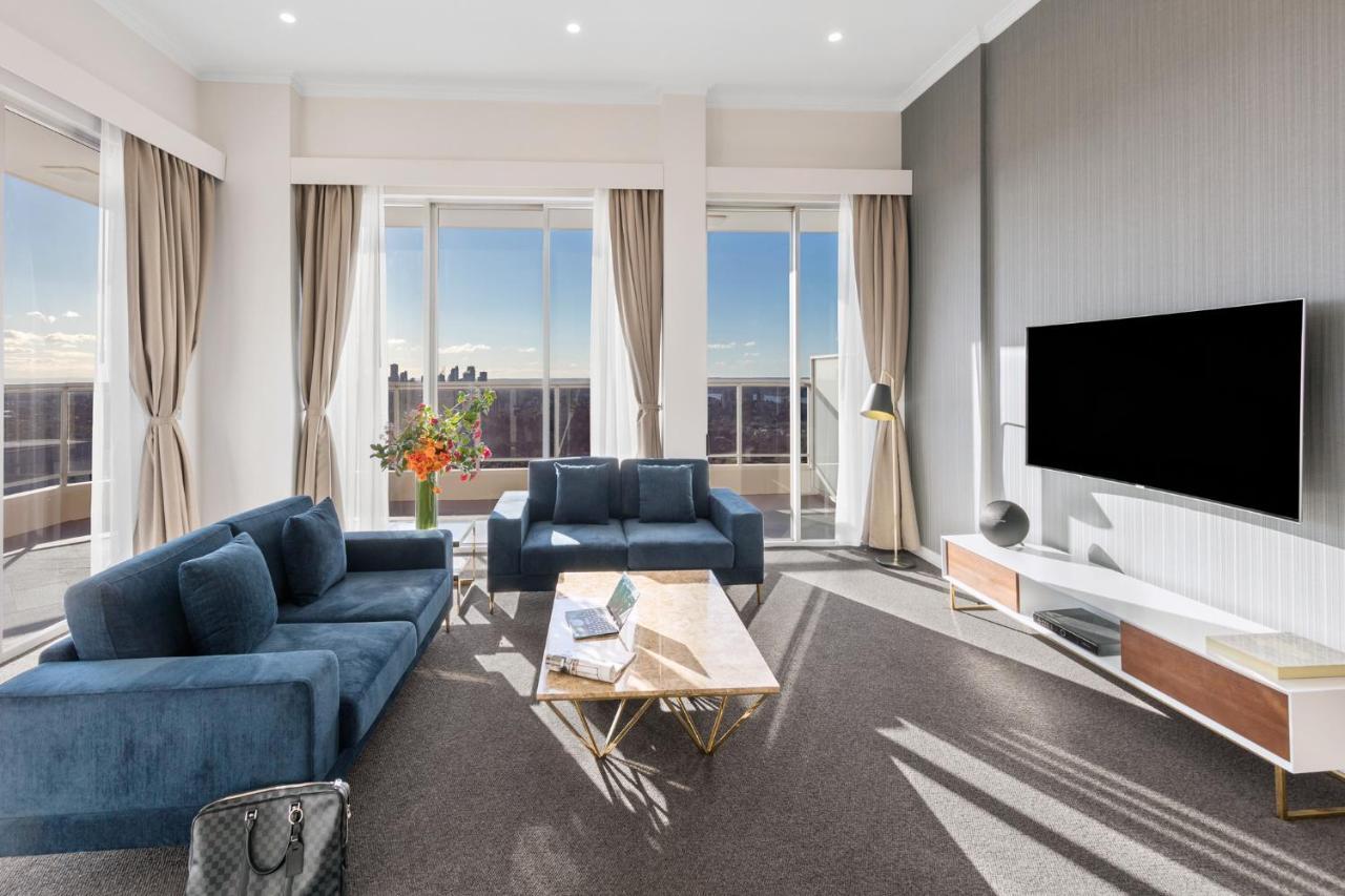 Meriton Suites Bondi Junction Sydney Luaran gambar The photo depicts a modern living room with a stylish and contemporary design. It features a cozy seating arrangement with a blue sofa and two matching armchairs. In front of the seating area is a coffee table with a geometric design. The room has la