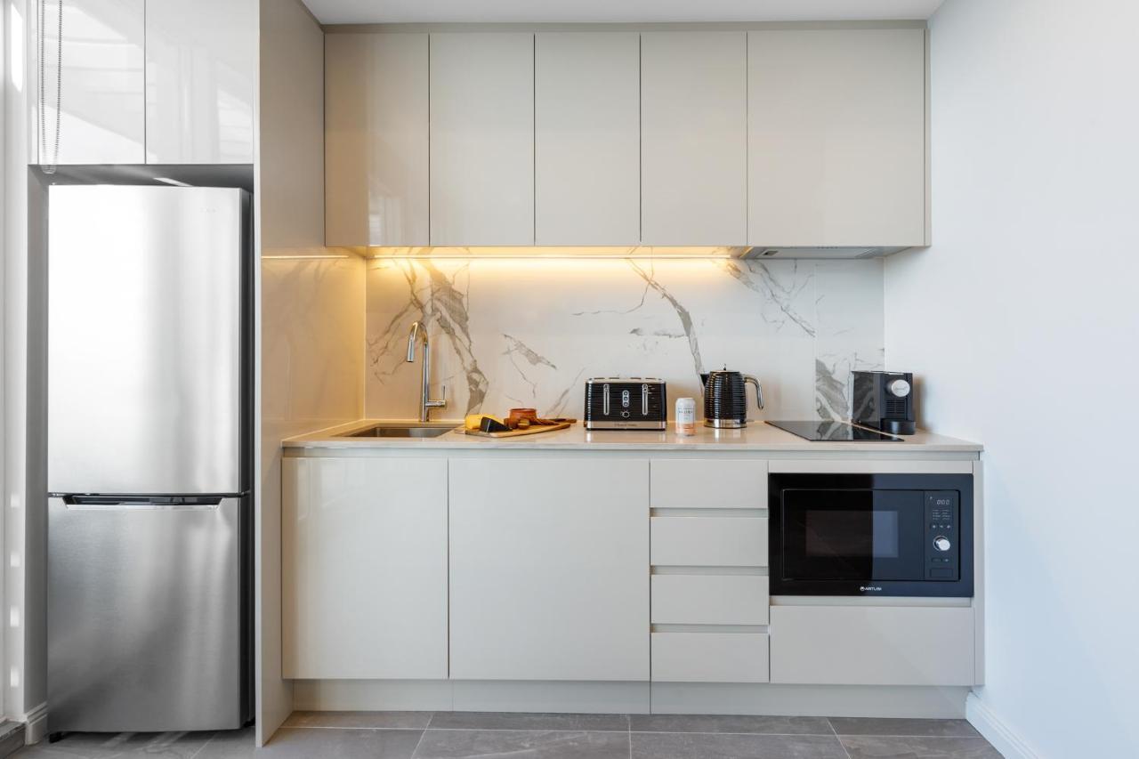 Meriton Suites Bondi Junction Sydney Luaran gambar The photo shows a modern kitchen featuring a sleek design. It includes light-colored cabinetry with a smooth finish and upper cabinets that blend seamlessly with the wall. The countertop is made of a light stone, complementing the overall aesthetic. 