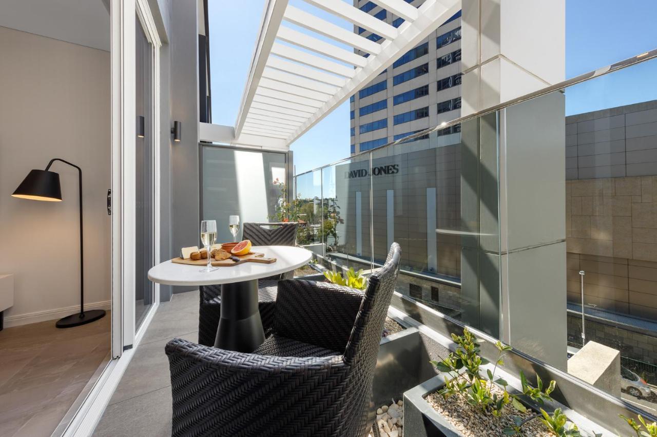 Meriton Suites Bondi Junction Sydney Luaran gambar The photo shows a modern balcony area with glass railings. It features a small round table set for two, with a plate of food and drinks. There are two stylish wicker chairs positioned around the table. The space is bright and airy, with sunlight stre