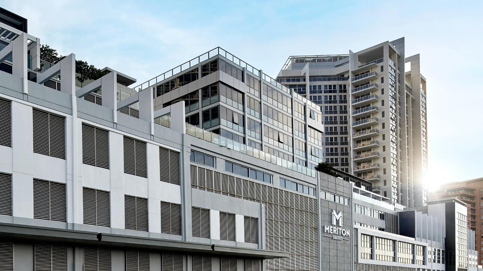 Meriton Suites Bondi Junction Sydney Luaran gambar The image shows a modern urban building or complex. The structure features a combination of glass and concrete elements, showcasing contemporary architectural design. The foreground has a lower section that appears to be a podium or base with a textu