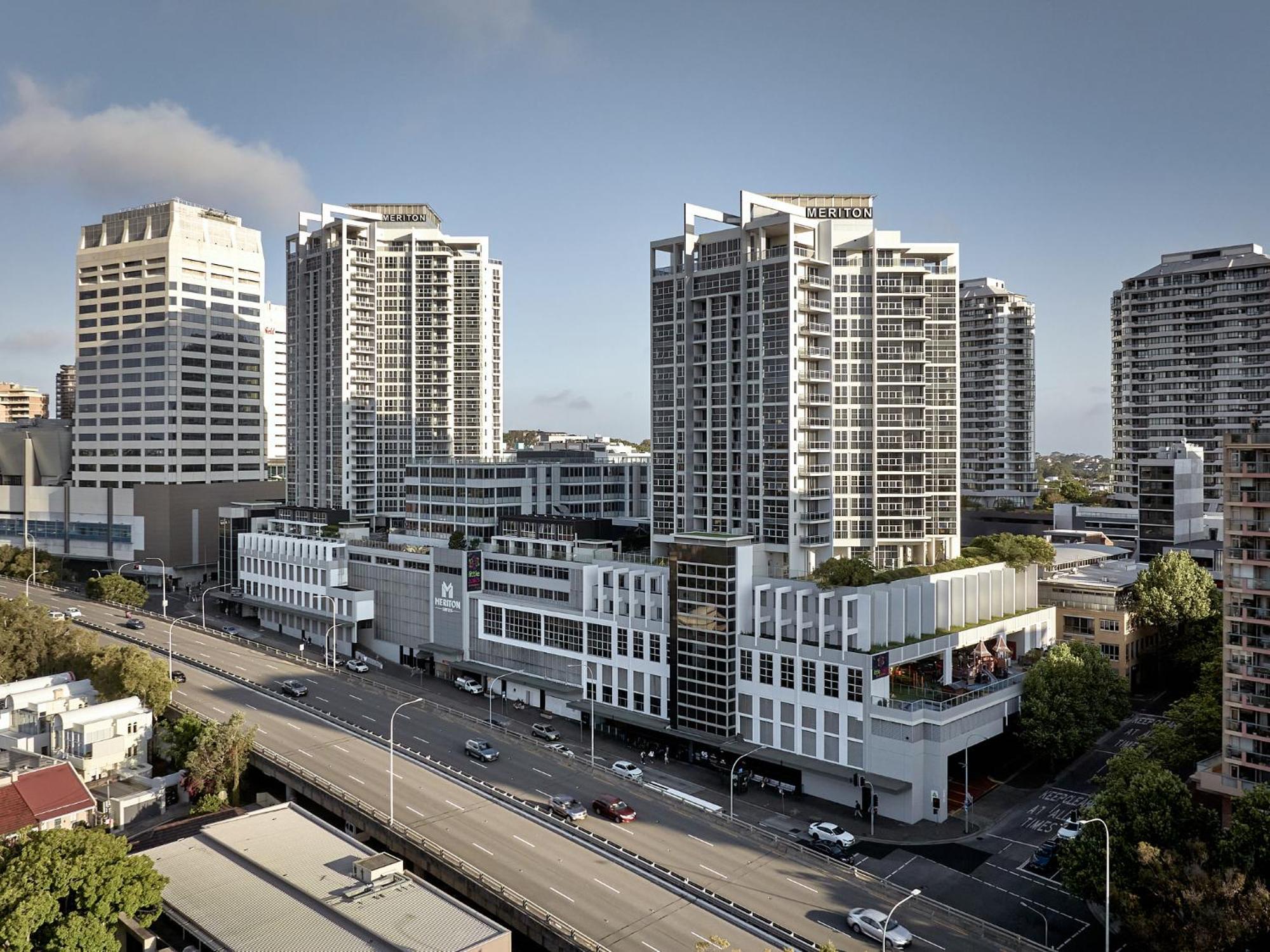 Meriton Suites Bondi Junction Sydney Luaran gambar The photo shows a cityscape featuring several tall modern buildings, likely apartments or office complexes. In the foreground, there is a road lined with cars, and the architecture of the buildings varies, with some having sleek glass facades and oth
